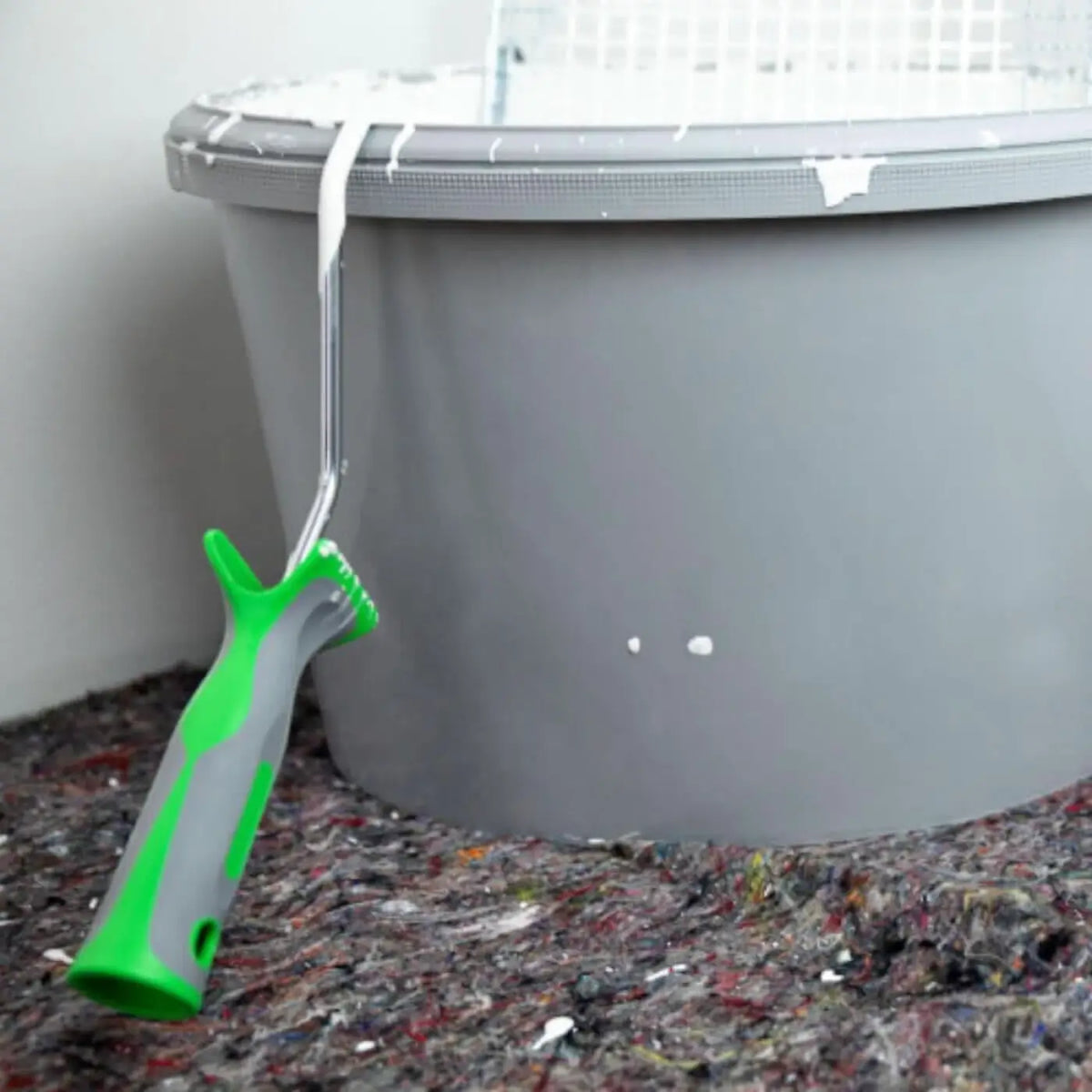 Grün-grauer malerroller mit metallstange lehnt an grauem plastik Eimer beim abdeckvlies basic 200 g/m²