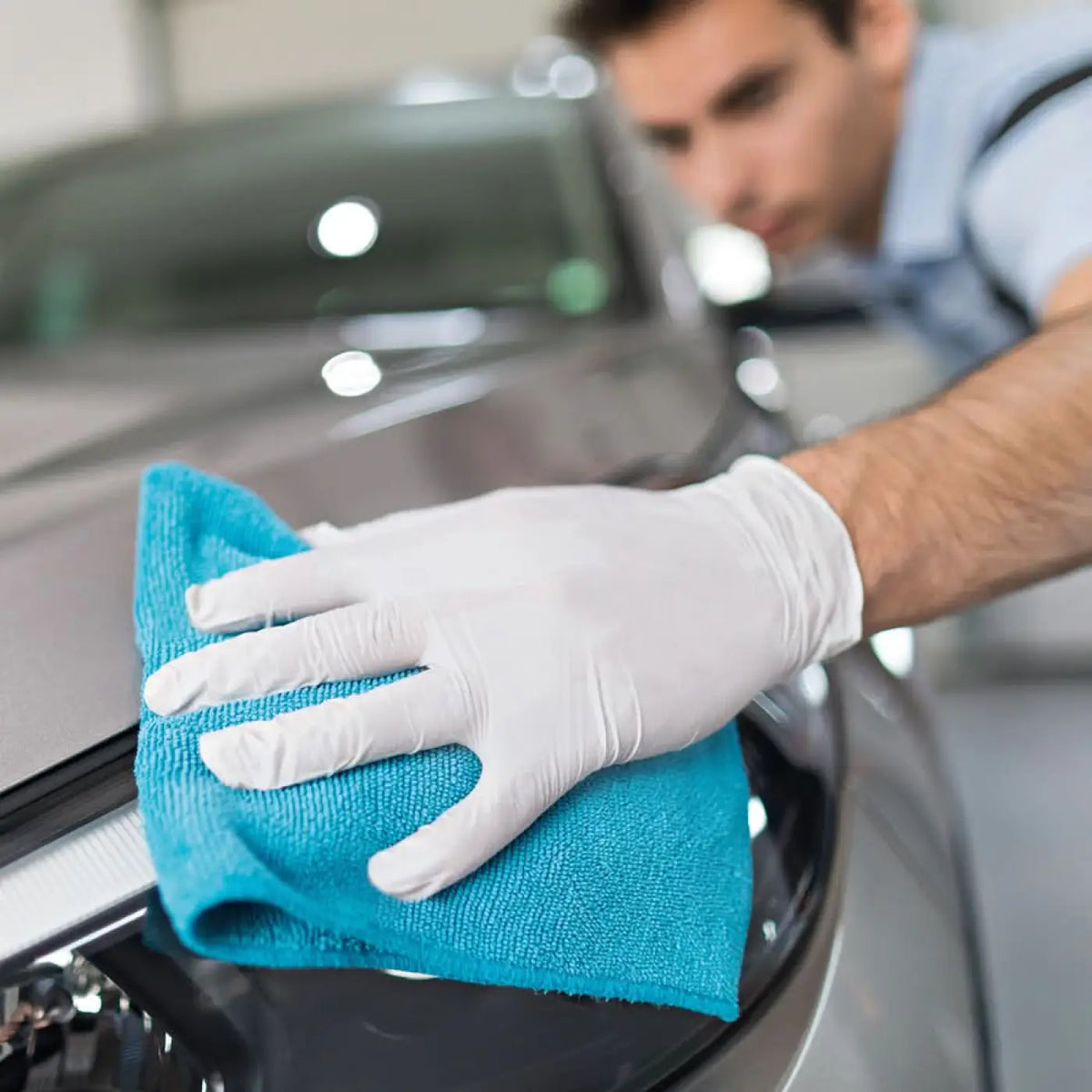 Hygostar safe premium weiße nitril handschuhe beim reinigen einer glänzenden schwarzen autofläche mit blauem microfiber tuch