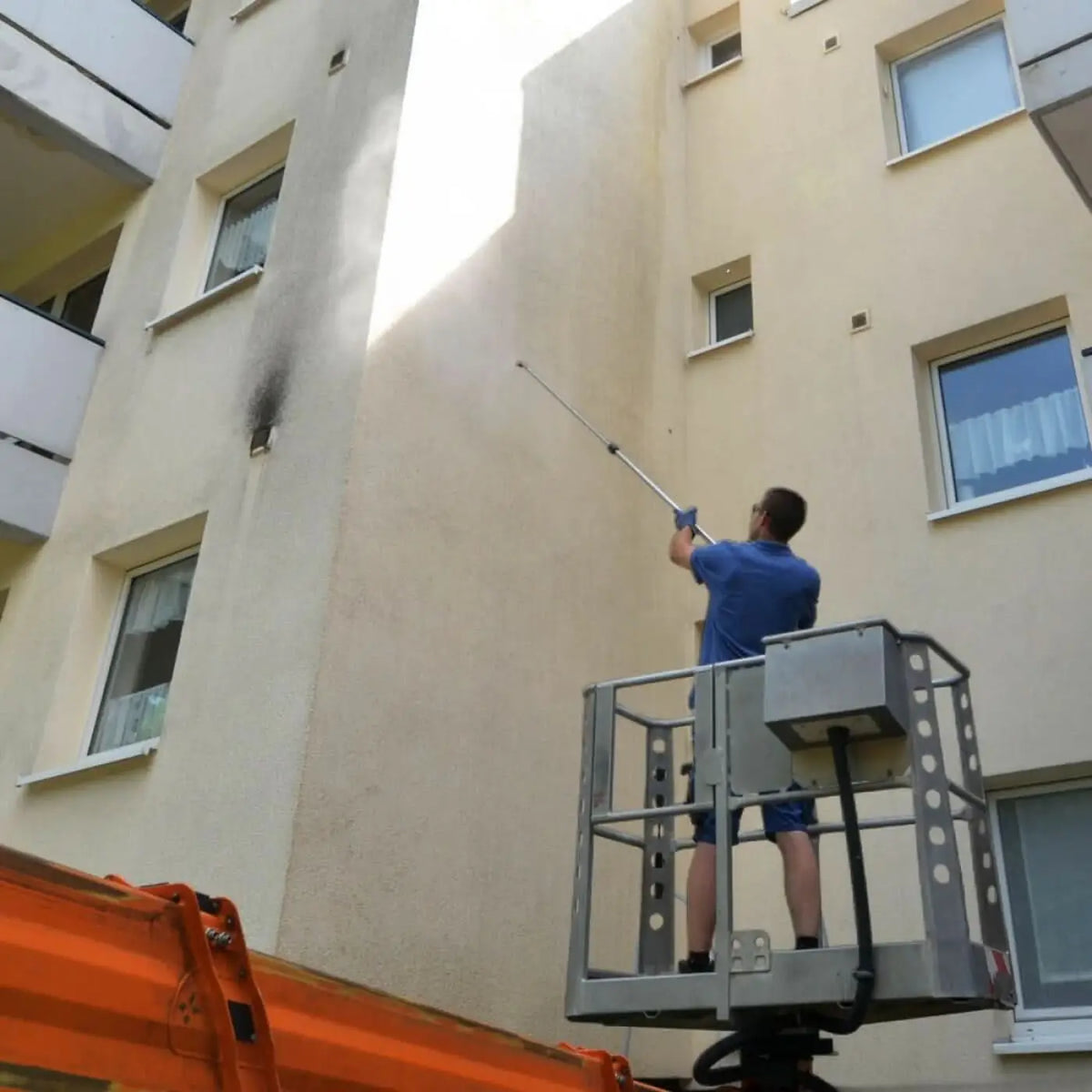 Ein arbeiter in blauem hemd bedient die silberne teleskoplanze T2 von HERMES Chemie zum reinigen einer gebäudefassade