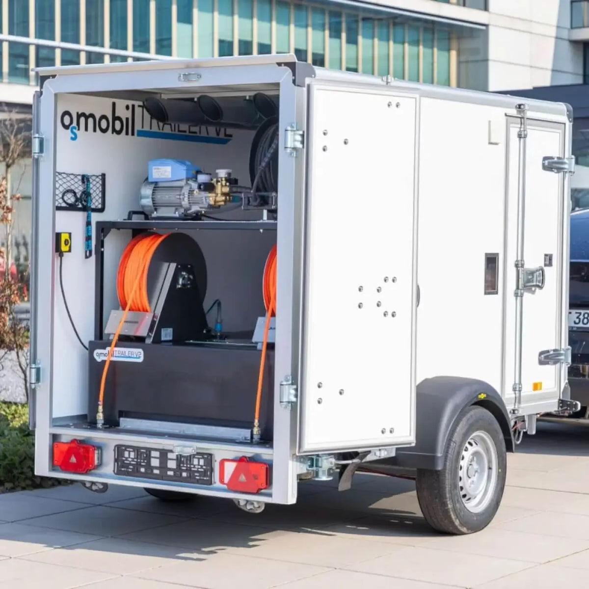 Weißer osmobil trailer v2 utility anhänger mit silbernem rahmen und orangen schweißschläuchen innen industrialausrüstung