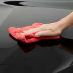 Ein rotes mikrofasertuch wischt eine glänzende schwarze oberfläche mit sonax autopolitur mit carnauba