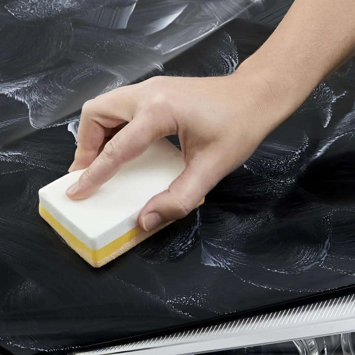 Weißer und gelber doppelseitiger schwamm wird verwendet, um eine schwarze oberfläche mit sonax autopolitur mit carnauba zu reinigen