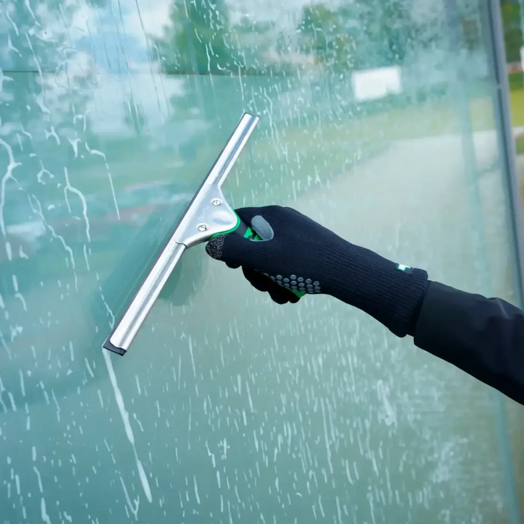 Unger ergotec glasreinigungshandschuhe mit silberner gummilippe und grün schwarzem ergonomischem griff am glas genutzt