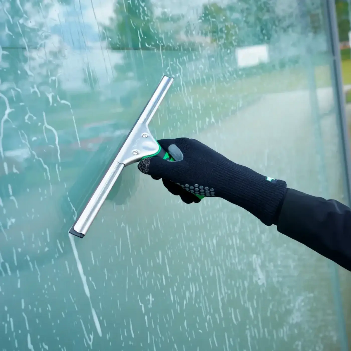 Unger ergotec glasreinigungshandschuhe mit silberner gummilippe und grün schwarzem ergonomischem griff am glas genutzt