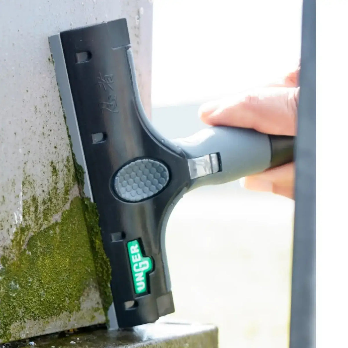 Black and gray unger Kunststoffklingen squeegee with textured grip handle used to remove green moss from surface